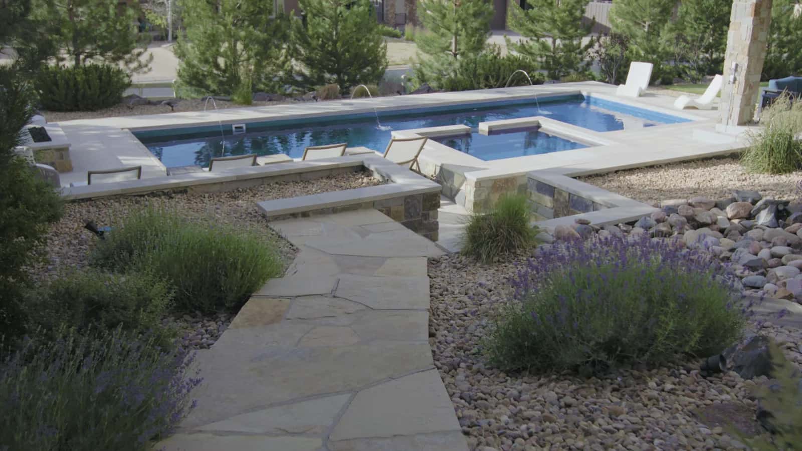 Zamucen Residence backyard: custom pool with laminar deck jets and raised spa, natural flagstone path, stone-veneer columns, and lavender plantings in Colorado