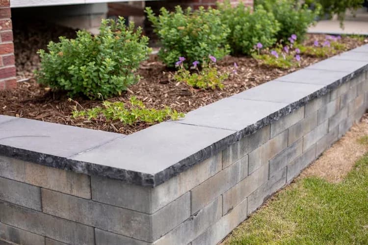 Segmental block retaining wall with dark capstone, mulch, shrubs, and purple accents along the walk, Westminster front yard.