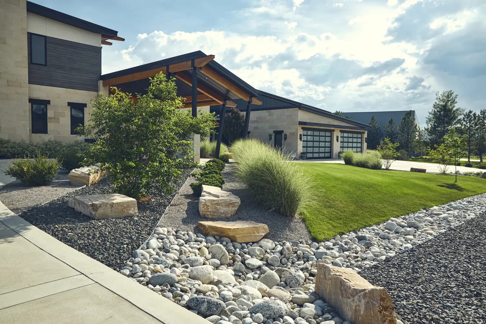 Front walk lined with sandstone boulders, ornamental grasses, and lawn leading to a modern entry, Colorado