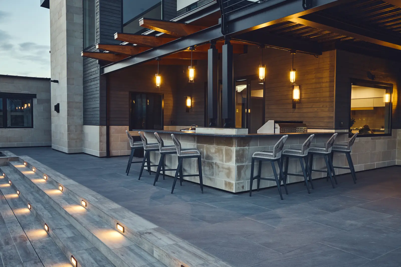 Outdoor bar with pendant lights and stools under the pergola at dusk, Johnson Estate, Colorado