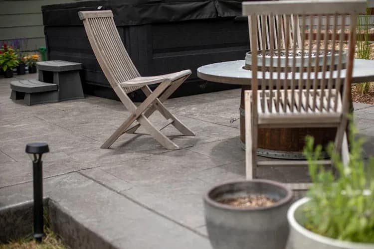 Gas fire pit table with wooden sling chairs on stamped concrete in one of the backyard gathering zones