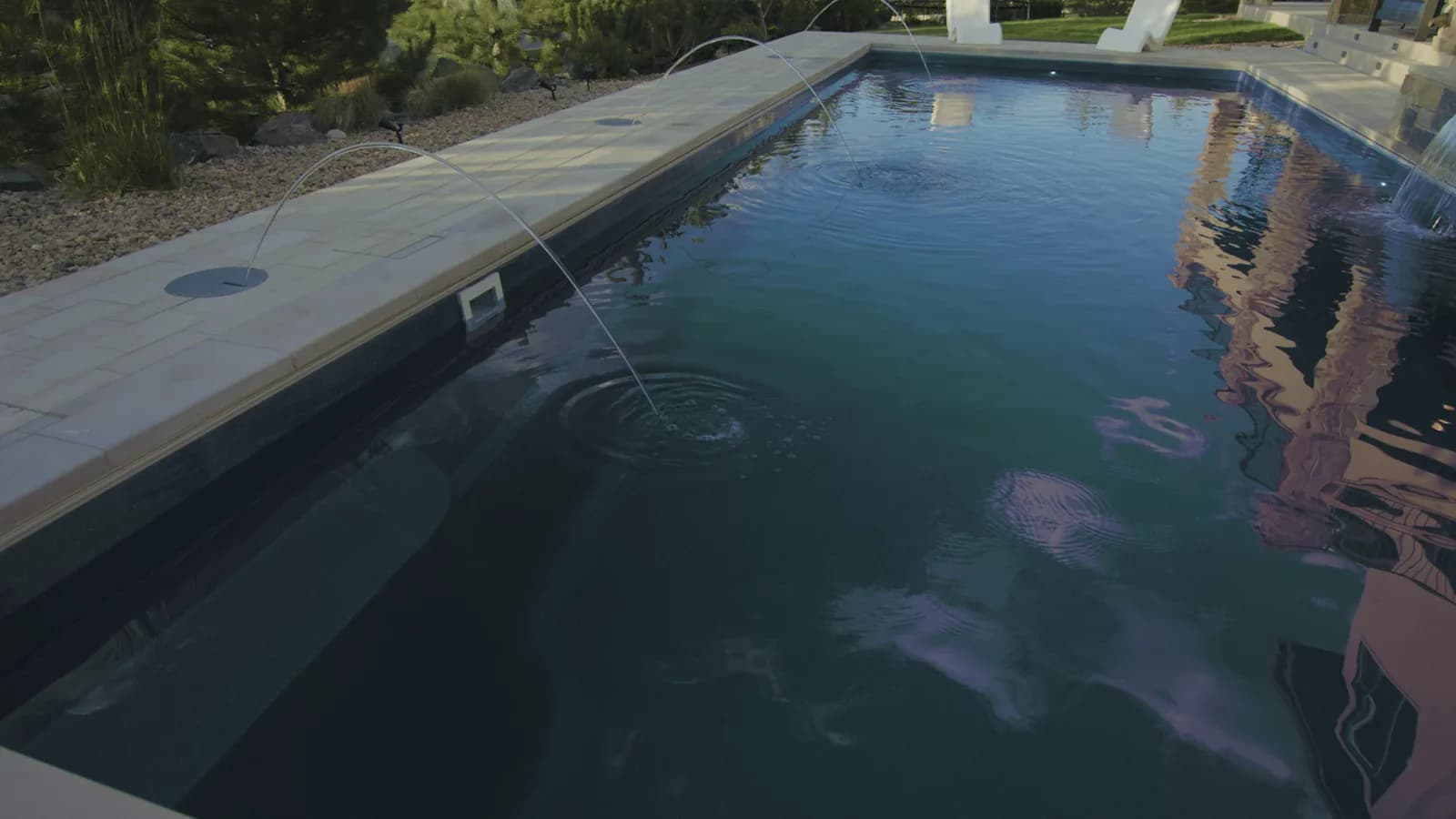 Laminar deck jets arcing over clear pool water with natural-stone coping and a tanning ledge at the Zamucen Residence in Colorado