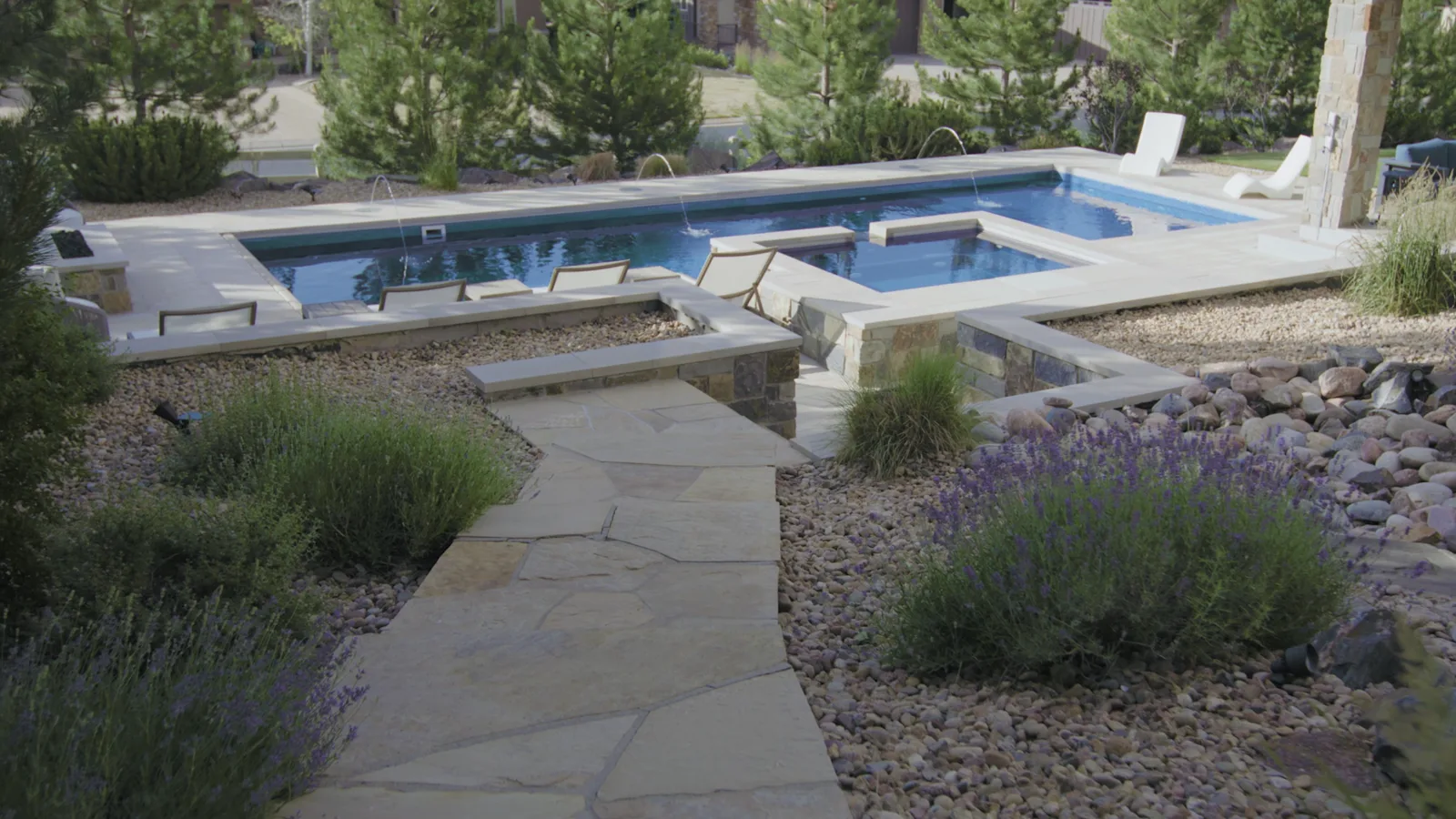 Zamucen Residence backyard: custom pool with laminar deck jets and raised spa, natural flagstone path, stone-veneer columns, and lavender plantings in Colorado