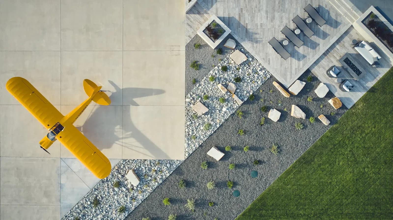 Aerial view of a private airplane parked beside a paver patio and boulder landscape at a Colorado airpark estate