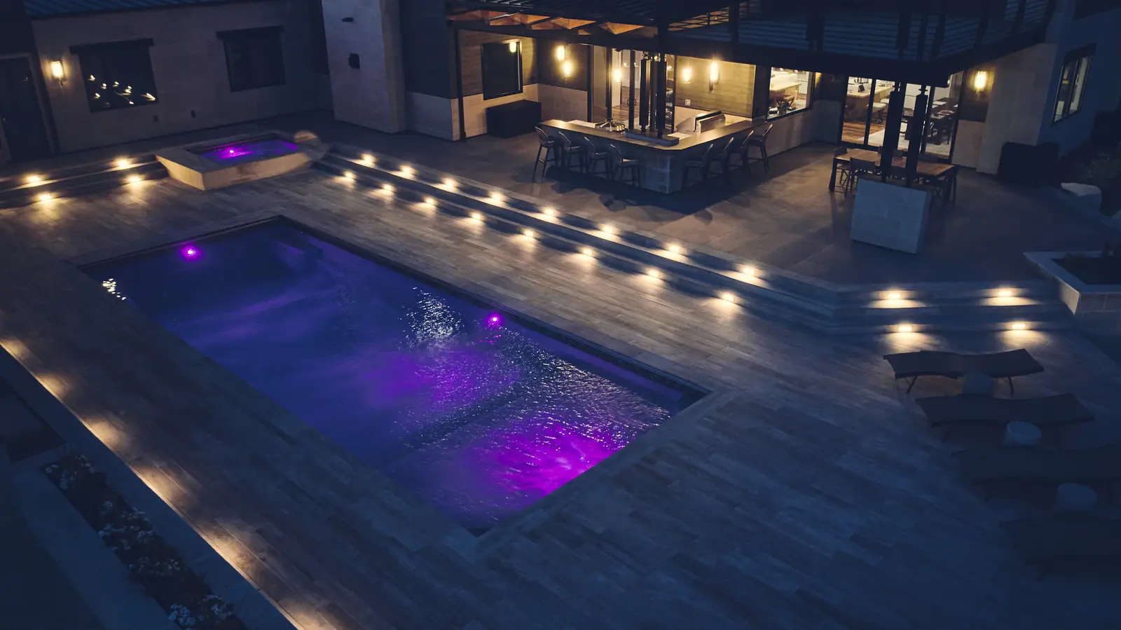 LED-lit pool at night with an illuminated outdoor kitchen and bar in the background
