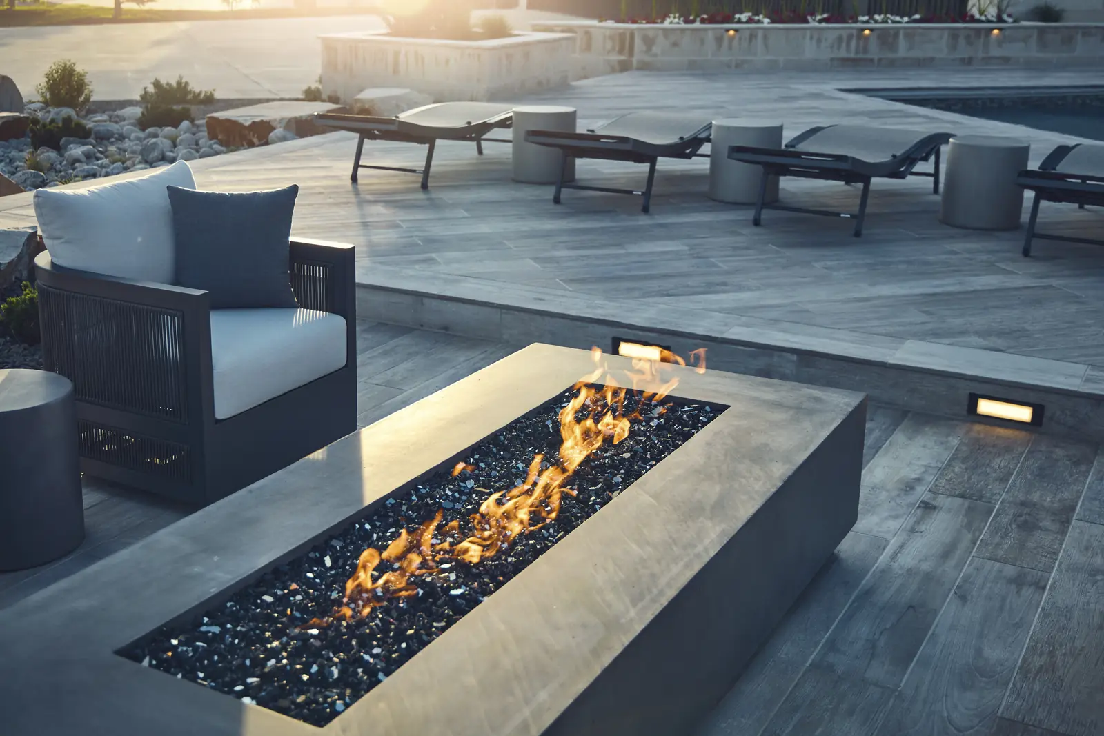 Flames rising from a linear concrete gas fire pit beside outdoor armchairs on a porcelain paver deck, Johnson Estate